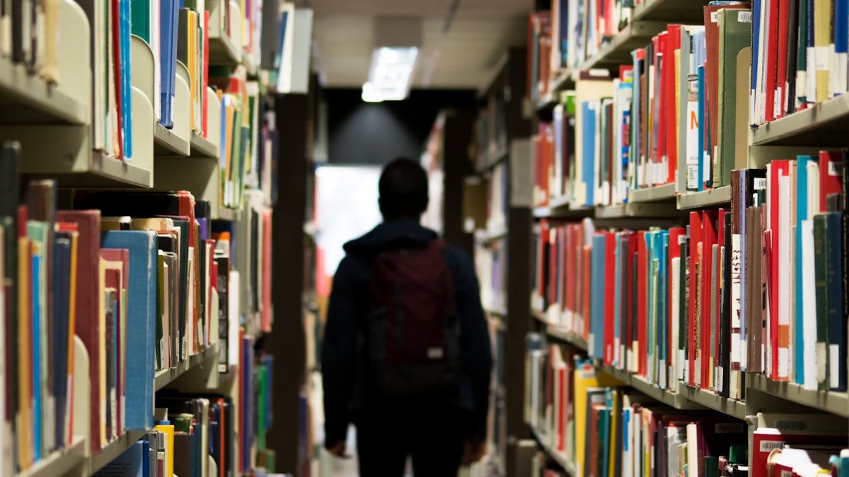 学びの悩みを調べる図書館の書棚と学習者の後ろ姿