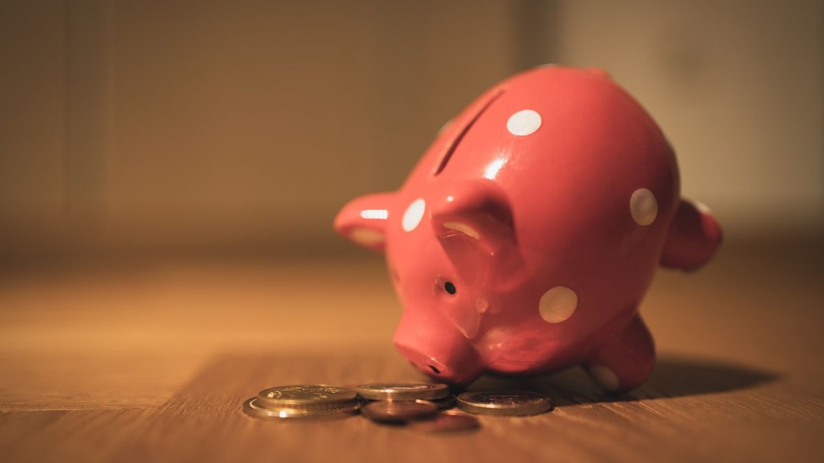 木の床に置かれたピンクの貯金箱と数枚の硬貨。支払いの仕組みを表すイメージ