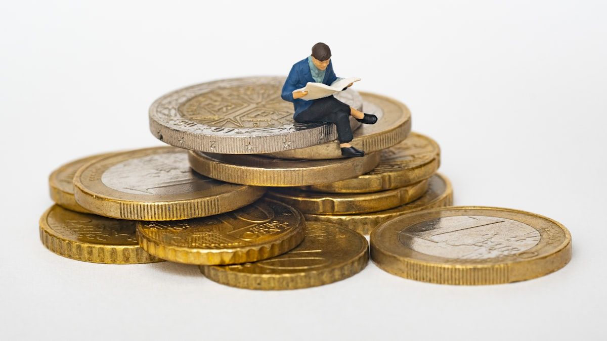 投資の使いどころを考えることを象徴する、硬貨の上で本を読むミニチュア