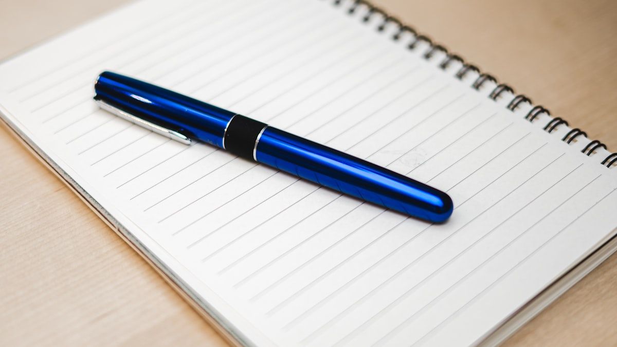 机の上のノートに置かれたペン。狙った言葉を書き出して次の一手を決めるイメージ