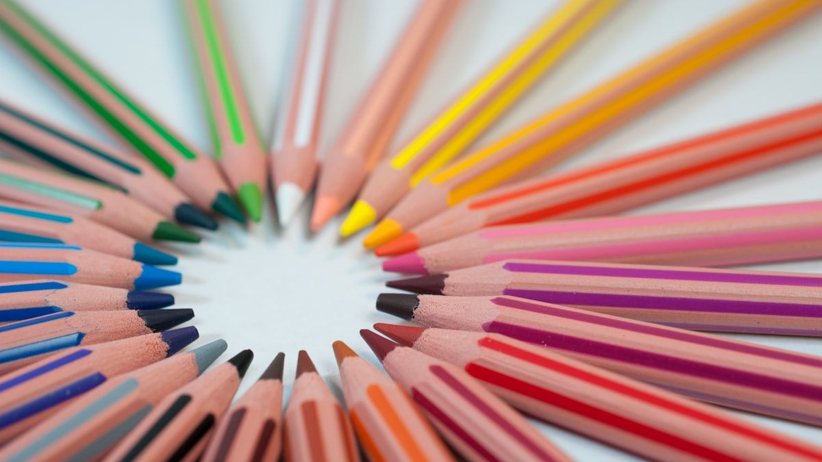 白い机の上に円を描くように並べられた色とりどりの色鉛筆。多くの候補が並ぶ様子のイメージ