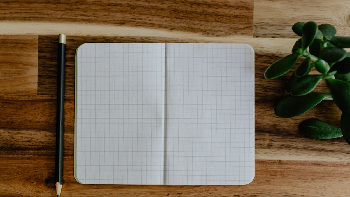 表記ゆれの候補を書き出すために木の机に置かれた方眼ノートと鉛筆